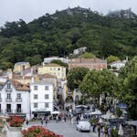 Vibrant street scene in Sintra, Portugal, showcasing colorful buildings and the Moorish Castle on a lush hillside.